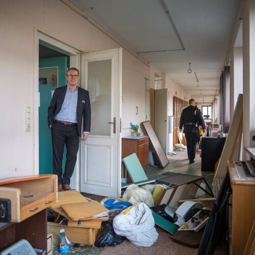 Vermieter steht in leerer Wohnung und blickt auf Müll und Möbel nach Räumung, während Vollstrecker den Flur verlässt.Vermieter steht in leerer Wohnung und blickt auf Müll und Möbel nach Räumung, während Vollstrecker den Flur verlässt.