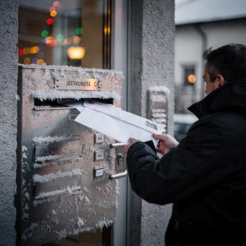 Ein dicker Briefumschlag wird bei Dämmerung hastig in einen frostigen Briefkastenschlitz geschoben.