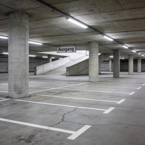 Eine weitläufige, rissige Betonfläche eines kühlen Parkdecks mit weißen Markierungen und massiven Betonpfeilern.